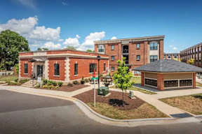 A red brick building with a black roof and a green tree in front.