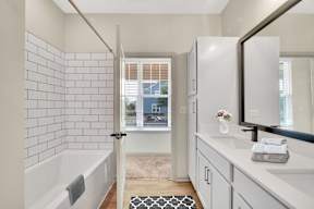 A bathroom with a white tub, sink, and a black and white rug.