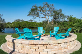 a fire pit with three adirondack chairs and a lake in the background