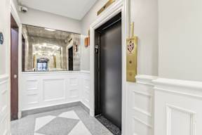 A hallway with a black elevator and a checkered floor.