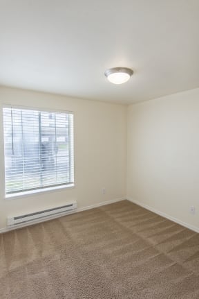 an empty bedroom with a large window and beige carpet