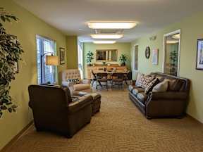 A living room with a brown couch, a chair, and a dining table with chairs around it.