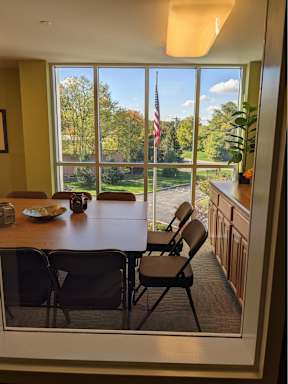 A dining room with a table and chairs and a view of the outdoors through a large window.