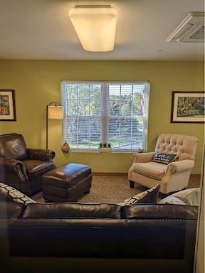 A living room with a brown leather couch, a brown leather chair, and a white chair with a throw pillow.
