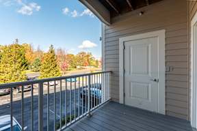 A balcony with a white door and a view of a parking lot and trees.