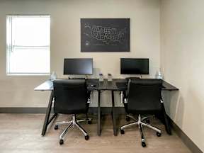 Two black computer desks with chairs and monitors in front of a wall with a map.