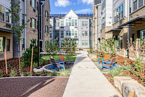 A walkway with benches and trees in front of apartment buildings.
