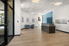 A reception area with a wooden desk and blue chairs.
