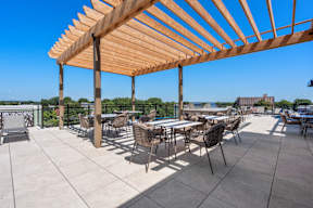 A wooden pergola over a patio with chairs and tables.