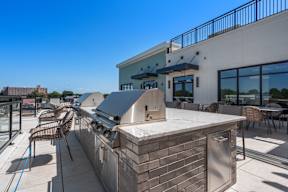 A rooftop patio with a barbecue grill and chairs.