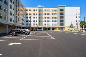 A parking lot in front of a multi-story building with cars parked.