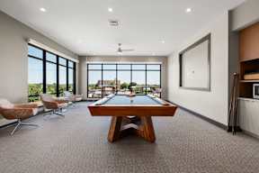 A billiard table is in the middle of a room with a ceiling fan and a large window.