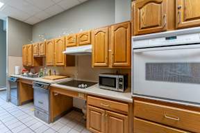 a kitchen with wooden cabinets and a stove and a microwave in the community room