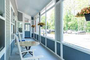A white rocking chair is on a porch with a table and a hanging flower basket.