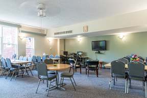 A room with tables and chairs and a television on the wall.