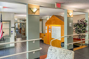 A hallway with a red exit sign and a wooden house-shaped object.