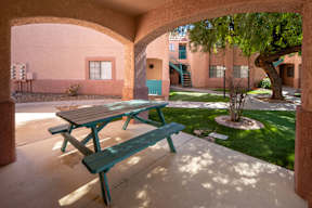 A picnic table and bench are in a courtyard with a tree and building in the background.
