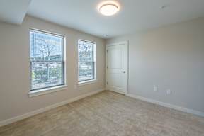 A room with a carpeted floor, a door, and two windows.