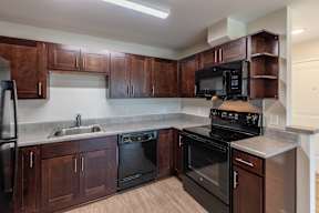 A kitchen with dark wood cabinets and black appliances.