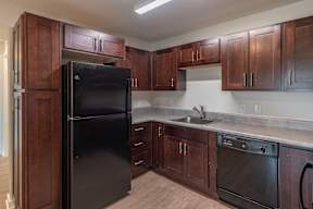 A black refrigerator stands in a kitchen with wooden cabinets.