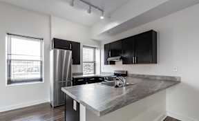 A modern kitchen with a stainless steel refrigerator and black cabinets.
