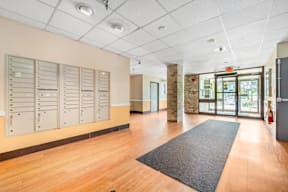 A hallway with a row of lockers on the left and a black mat on the floor.