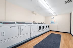 A row of washing machines numbered 5 to 7 are lined up in a laundry room.