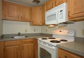A kitchen with a white microwave oven mounted above a white gas stove.