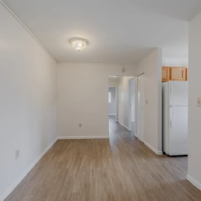 A white room with a refrigerator and wooden flooring.