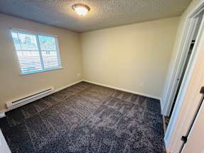 A room with a carpeted floor and a window with blinds.