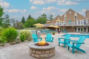 a fire pit with blue adirondack chairs and umbrellas in front of a