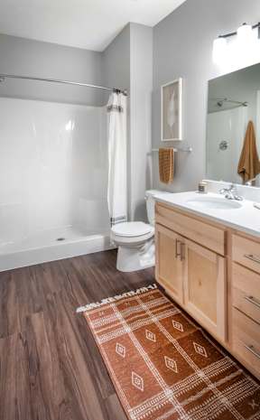 A bathroom with a white tub and toilet, a brown rug, and wooden cabinets.