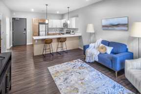 A modern living room with a blue couch and a kitchen area in the background.