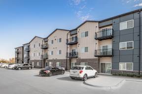 A row of modern apartment buildings with cars parked in front.