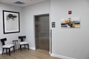 Two chairs and a table are in a room with a framed picture on the wall.
