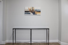 A painting hangs on a wall above a black metal table with a white top.