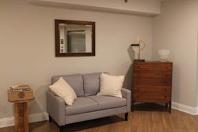 A grey couch with a white pillow sits in front of a mirror.