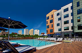 A pool area with chairs and umbrellas in front of a multi-story building.