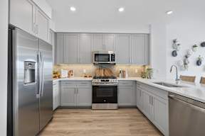 A modern kitchen with a stainless steel refrigerator and wooden flooring.