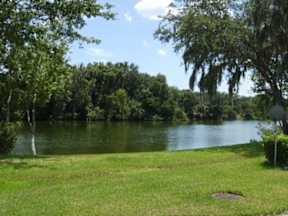 a grassy area with a lake in the background  at Waters Edge Apartments, Lakeland, FL, 33803