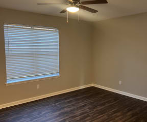 an empty living room with a large window and a ceiling fan