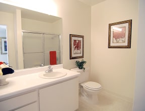 a white bathroom sink with white cabinets and white coutertops and a white toilet located on the right a large mirror sits in the front of the sink and some decorating accents, Prodesse Property Group