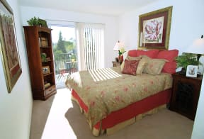 The bedroom with a large queen size bed with red and tan bedding the window leads to a bedroom patio outside a unit at Prodesse Property Group 1211 Garbo Way  San Jose, CA 95117