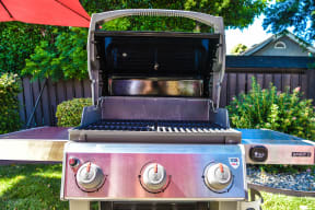 a stainless steel grill in a backyard with a red umbrella in the background