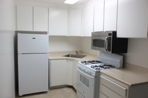 The white kitchen with white cabinets a white fridge, white stove and stainless steel microwave