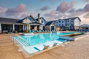a swimming pool with lounge chairs in front of an apartment building