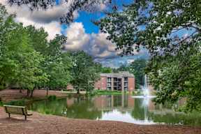 A serene park with a fountain, bench, and trees.