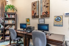 a desk with two computer monitors and two chairs in a room with a bookshelf and