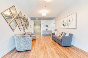 A living room with a grey couch, a grey ottoman, and a painting on the wall.