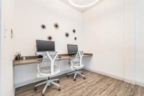 Two white chairs are positioned in front of two computers on a desk.